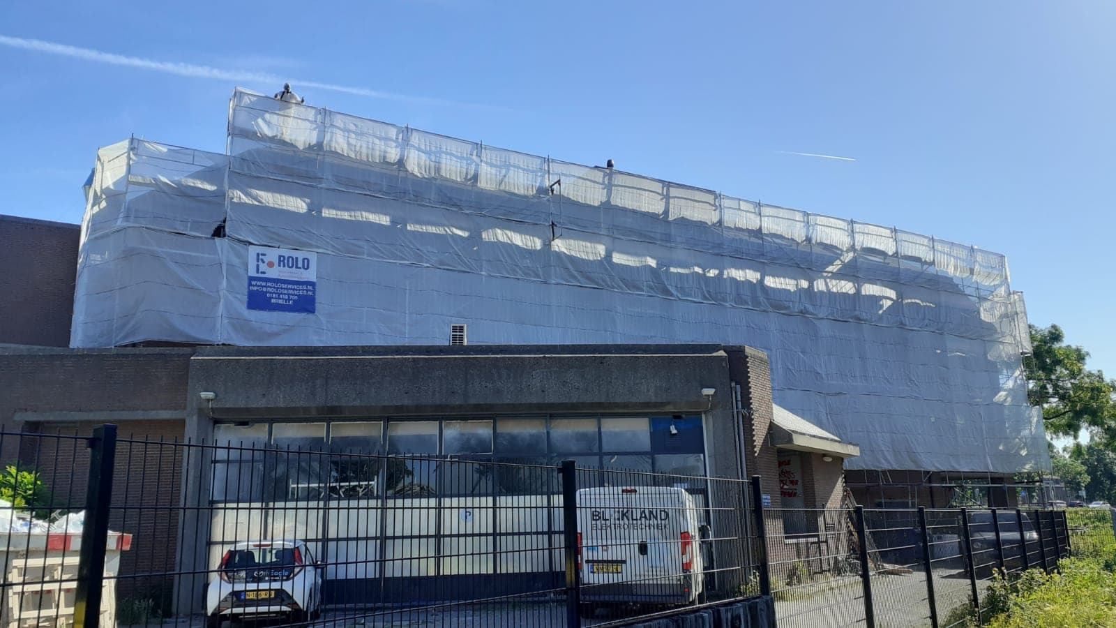 Gebouw in Schiedam ingepakt in steigers en folie voor het saneren van de daklijnen
