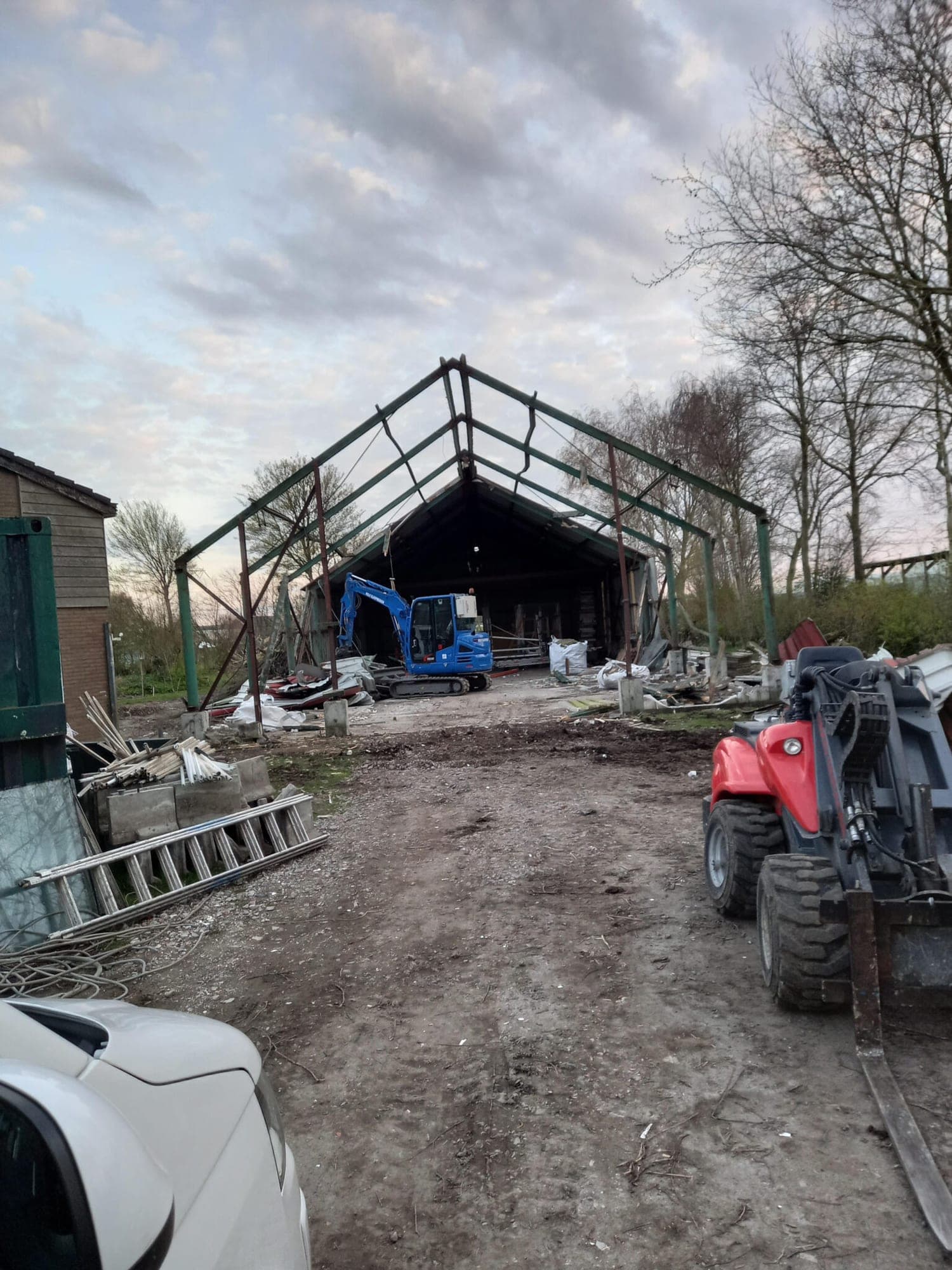 Blauwe minigraver sloopt een stalen loods